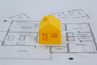設計図の上に置かれた黄色い三角屋根の家の模型