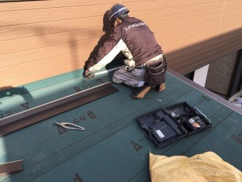張られているルーフィングシートの余分な所を切り落としている職人