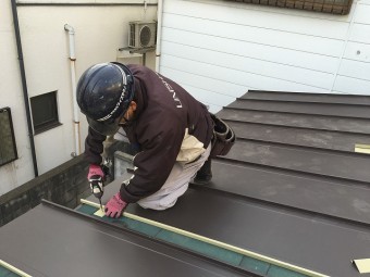 板金屋根材を屋根面に取り付けている職人