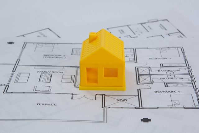 設計図の上に置かれた黄色い三角屋根の家の模型